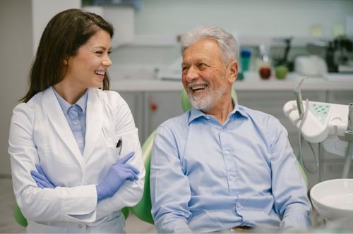 Dentist and elderly patient smiling during a restorative dentistry consultation at The Village Dental in Pinecrest, FL, emphasizing a positive dental care experience.