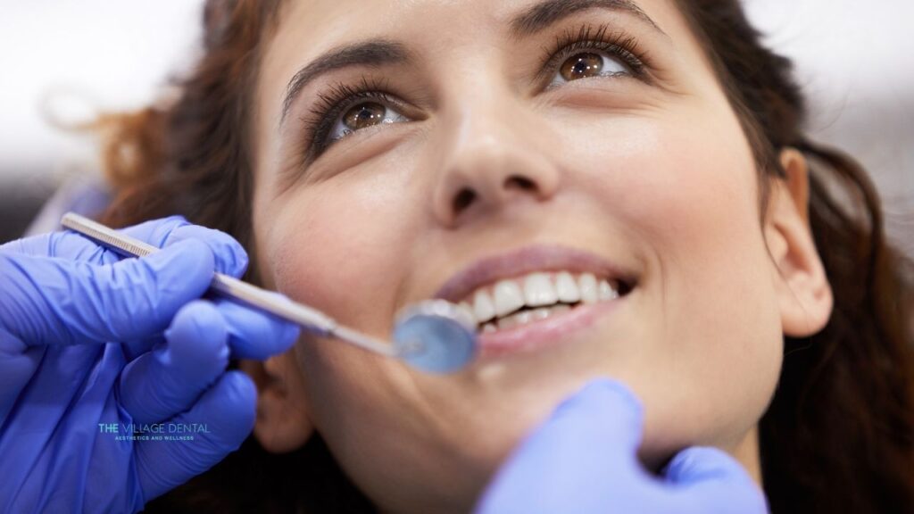 Patient receiving cosmetic dental treatment at The Village Dental in Pinecrest, FL, with a dentist using a dental tool to enhance smile aesthetics and health.