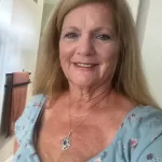 Smiling woman with long hair in a floral top, representing patient satisfaction at The Village Dental in Pinecrest, FL, highlighting a welcoming dental experience and professional care.