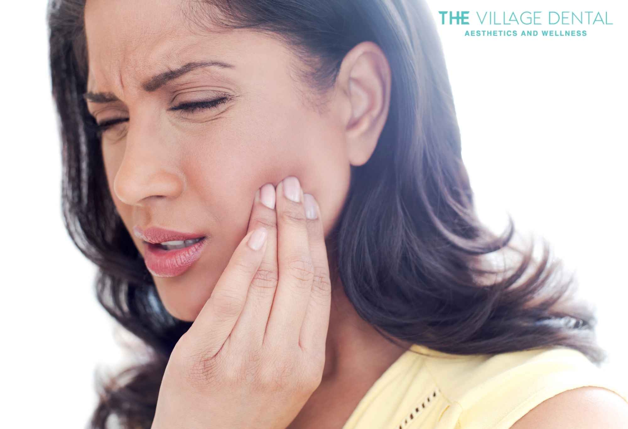 Woman experiencing dental pain, holding her cheek, representing urgent care needs at The Village Dental in Pinecrest, FL.
