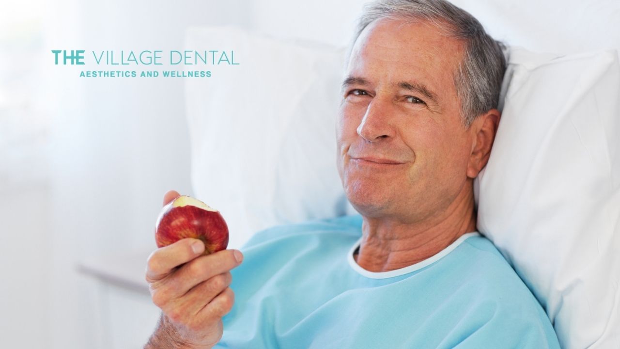 Senior man enjoying a fresh apple, showcasing restored chewing ability after dental implants from The Village Dental, Aesthetics and Wellness in Miami.