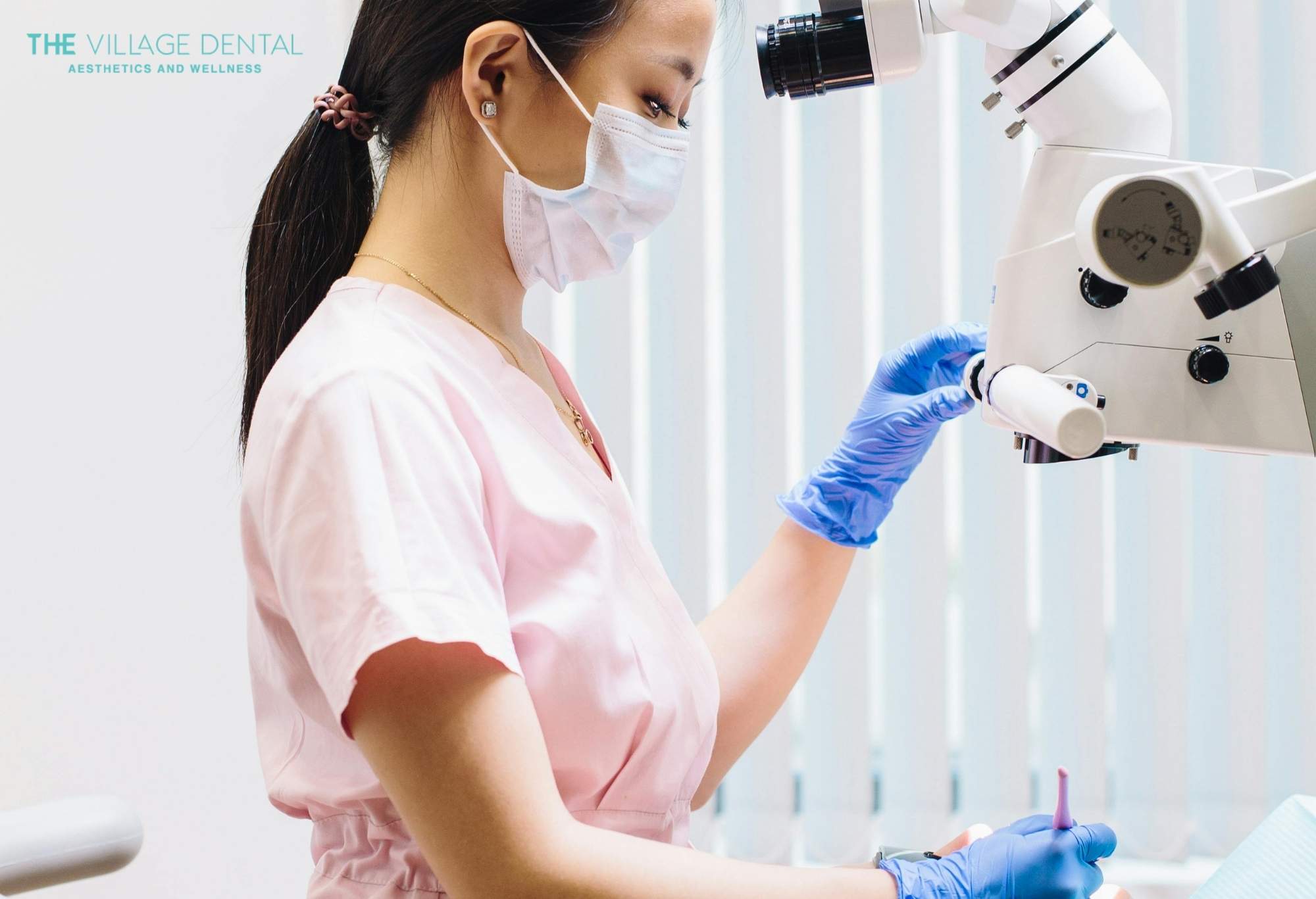Dental professional in pink scrubs and mask preparing dental equipment for root canal therapy at The Village Dental in Pinecrest, FL, emphasizing patient care and advanced dental techniques.