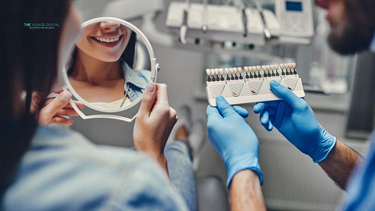Patient smiling in dental chair while dentist shows shade guide for cosmetic dental treatment at The Village Dental in Pinecrest, FL.