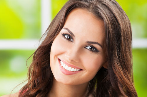Smiling woman with bright, white teeth in a spa-like dental office setting, representing cosmetic dentistry services at The Village Dental in Pinecrest, FL.