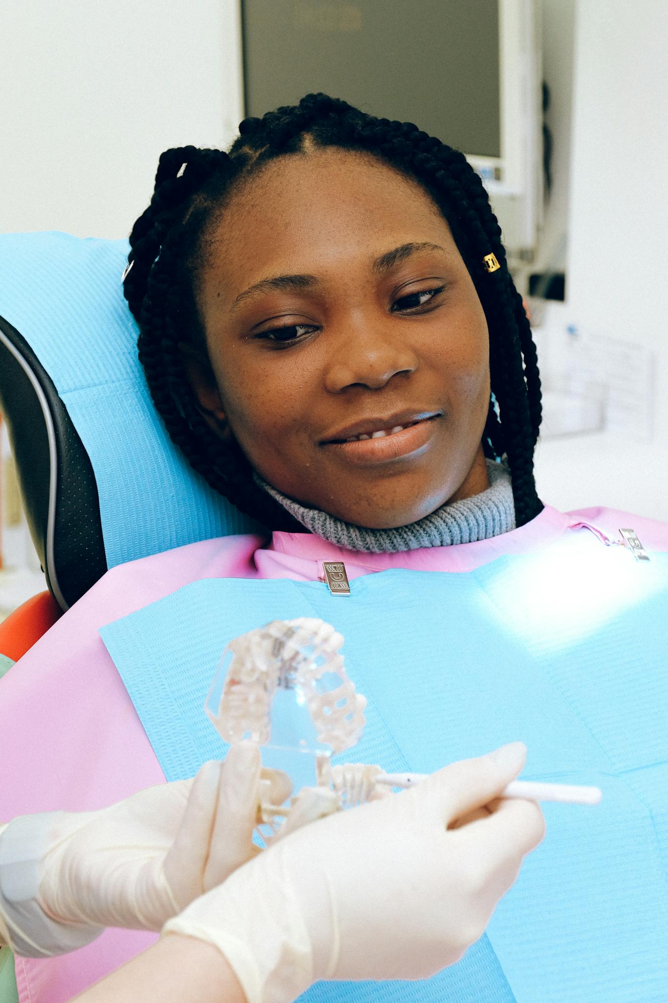 Woman smiling in a dental chair, wearing a pink bib, during a cosmetic dental consultation at The Village Dental, showcasing a positive patient experience in aesthetic dentistry.