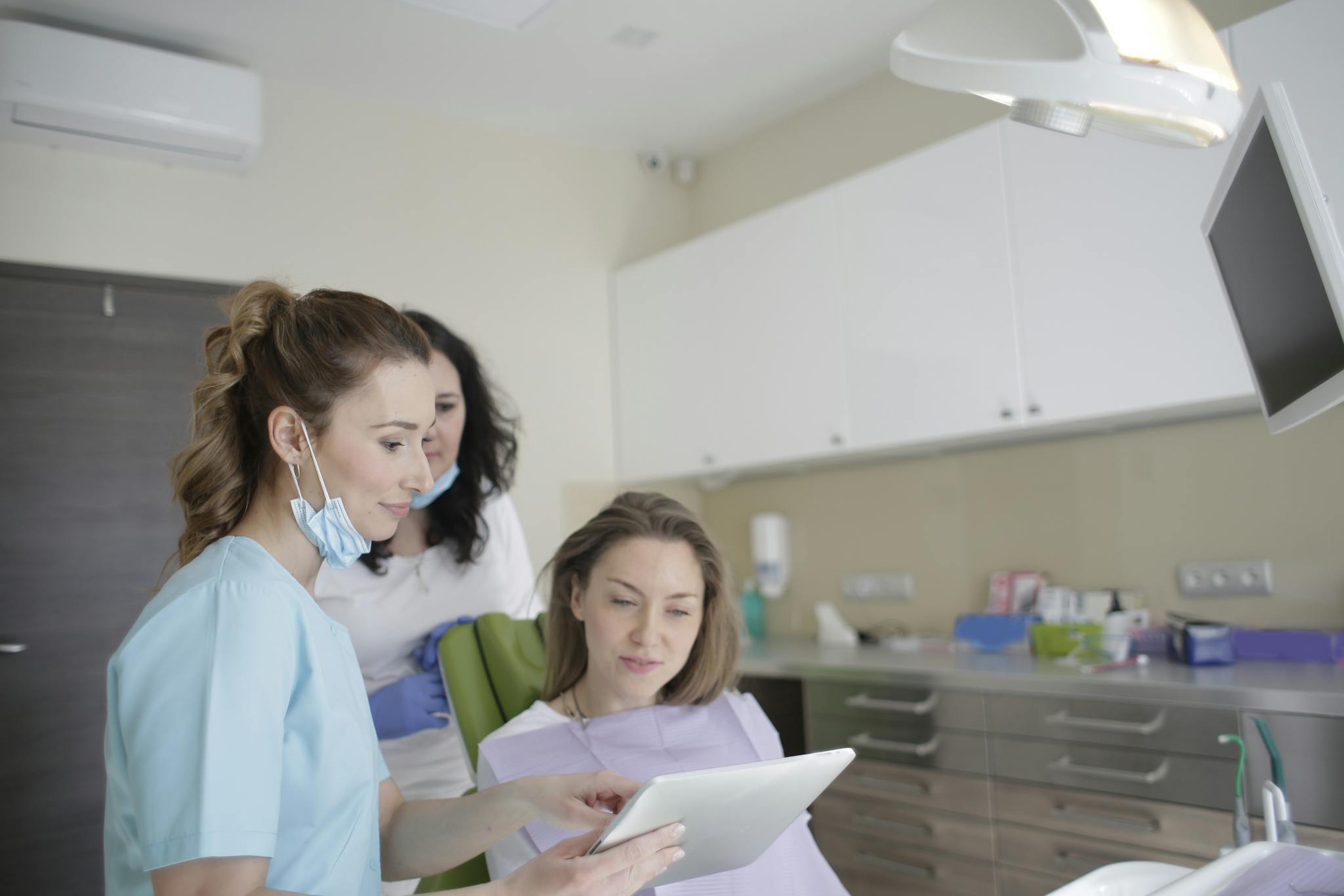 Dental professionals at The Village Dental in Pinecrest, FL, engaging with a patient, discussing treatment options using a tablet in a modern dental office setting.