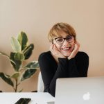 Smiling woman with glasses at a desk, showcasing a confident and happy expression, representing patient satisfaction at The Village Dental's cosmetic dentistry services in Miami.